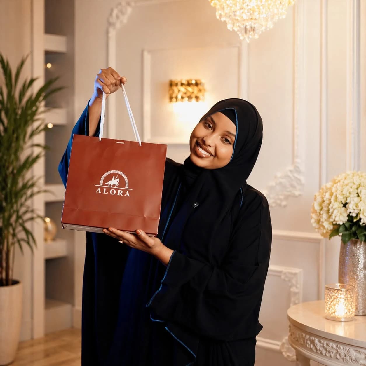 A smiling woman holding up a red ALORA gift bag